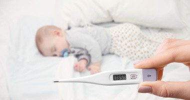 Kobieta trzyma termometr wskazujący wysoką temperaturę u dziecka z zespołem PFAPA