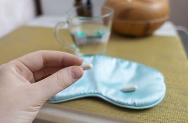 tabletka z melatoniną w dłoni i opaska na oczy, jak dawkować melatoninę na sen, suplementacja melatoniny, wpływ melatoniny na sen