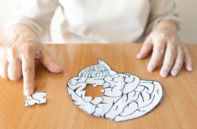Starsza kobieta ukłąda puzzle w kształcie ludzkiego mózgu, w których brakuje jednego elementu, na którym palec trzyma pacjentka