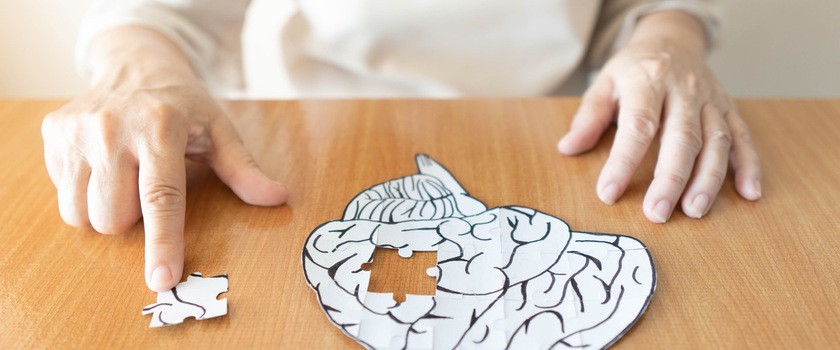 Starsza kobieta ukłąda puzzle w kształcie ludzkiego mózgu, w których brakuje jednego elementu, na którym palec trzyma pacjentka