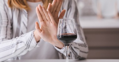 Kobieta wystawia dłonie przed kieliszek wina w geście braku chęci do spożycia alkoholu, Dry January