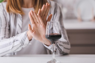 Kobieta wystawia dłonie przed kieliszek wina w geście braku chęci do spożycia alkoholu, Dry January