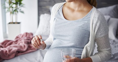 Kobieta w ciąży trzyma w dłoni tabletkę kwasu foliowego i kwasu foliowego metylowanego