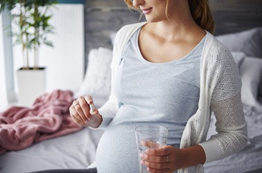 Kobieta w ciąży trzyma w dłoni tabletkę kwasu foliowego i kwasu foliowego metylowanego