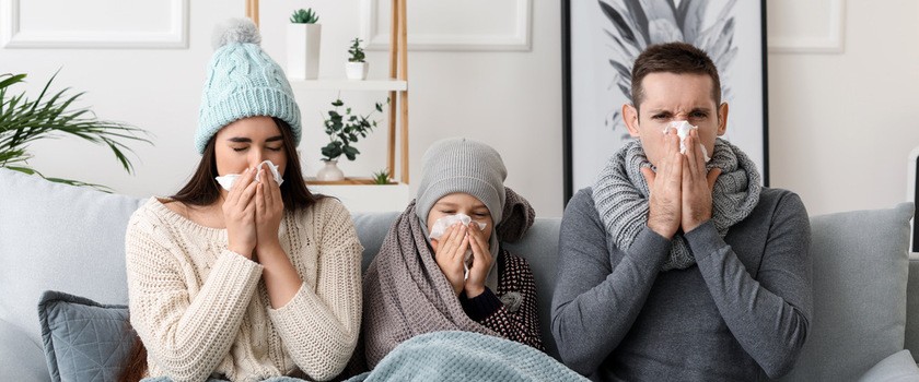 Rodzna chora na grypę siedzi na szarej kanapie