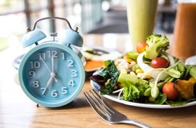 niebieski zegarek na drewnianym stole, na którym leży talerz z sałatką