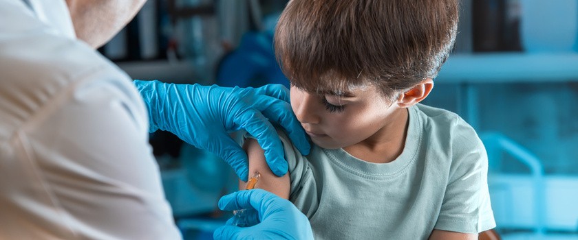 Chłopiec w niebieskiej koszulce dostaje dawkę szczepionki w ramię