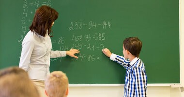 Dziecko przy tablicy w szkole z nauczycielką na lekcji matematyki