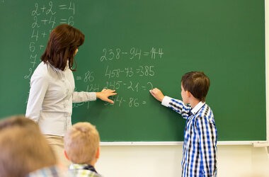 Dziecko przy tablicy w szkole z nauczycielką na lekcji matematyki
