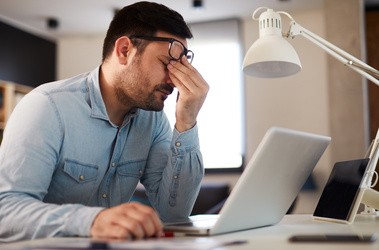 Przemęczony mężczyzna w stresie siedzi i pracuje przy laptopie