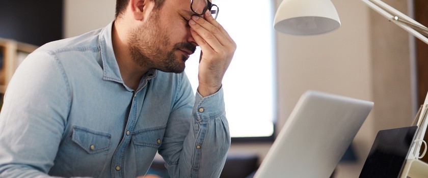 Przemęczony mężczyzna w stresie siedzi i pracuje przy laptopie
