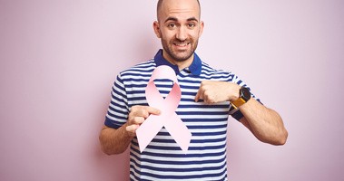Młody mężczyzna trzyma różową wstążkę raka piersi ze zdziwioną twarzą, wskazuje palcem na siebie