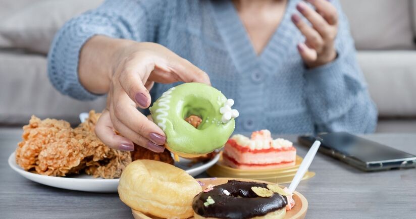ochota na coś słodkiego, łaknienie cukru, kobieta sięga po pączka do talerza z wypiekami