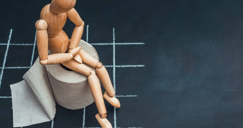 drewniana figurka siedzi na rolce papieru toaletowego