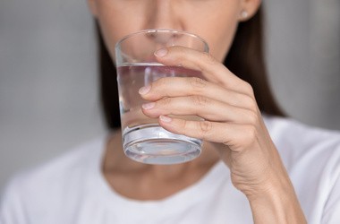 Młoda kobieta trzyma w dłoni szklankę wody - pije, aby uniknąć odwodnienia u dorosłych