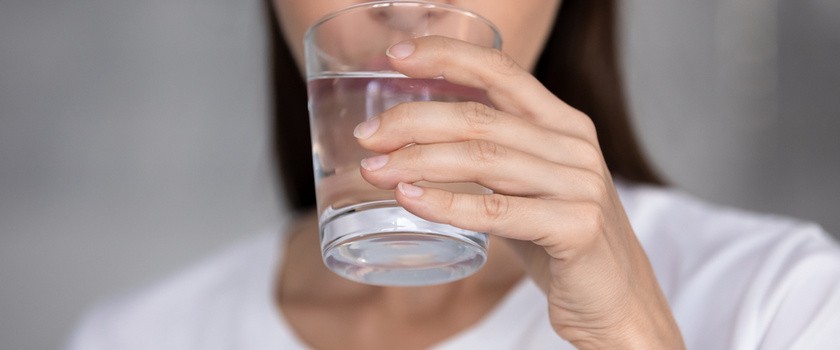 Młoda kobieta trzyma w dłoni szklankę wody - pije, aby uniknąć odwodnienia u dorosłych