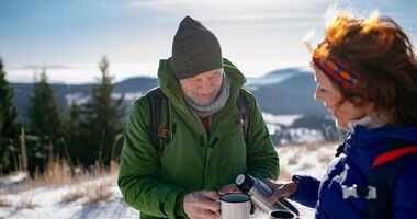 Osoby piją ciepłą herbatę podczas trekkingu górskiego zimą. Profilaktyka hipotermii, hipotermia, co to hipotermia, czym jest hipotermia, objawy hipotermii, wychłodzenie.