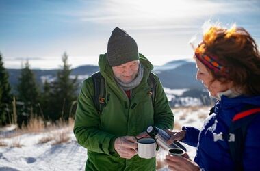 Osoby piją ciepłą herbatę podczas trekkingu górskiego zimą. Profilaktyka hipotermii, hipotermia, co to hipotermia, czym jest hipotermia, objawy hipotermii, wychłodzenie.