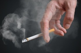 Palacz trzyma w ręku papierosa, z którego leci dym tytoniowy