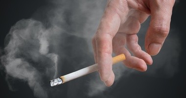 Palacz trzyma w ręku papierosa, z którego leci dym tytoniowy