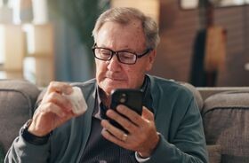 starszy mężczyzna z lekiem i telefonem w ręku, nowa lista leków refundowanych