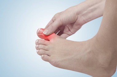 kobieta trzyma się za bolący duży palec u stopy
