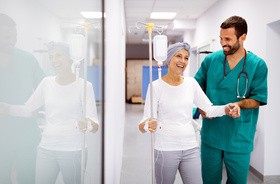 Kobieta podczas terapii onkologicznej i w towarzytwie lekarza, idzie korytarzem szpitalnym.