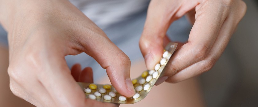 Kobieta w ciąży otwiera opakowanie tabletek antykoncepcyjnych