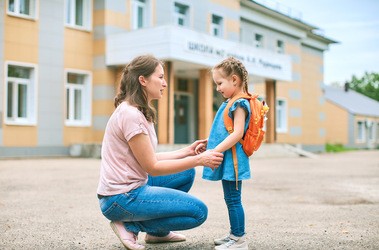 Dziecko wraz z mamą pierwszego dnia w przedszkolu, stoją przed budynkiem przedszkola i żegnają się