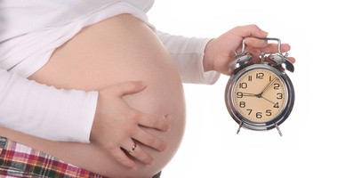 Kobieta ciąży na zdjęciu wraz z zegarkiem imitującym upływ czasu