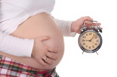 Kobieta ciąży na zdjęciu wraz z zegarkiem imitującym upływ czasu