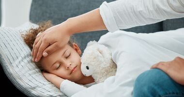 przeziębione dziecko śpi, a rodzic sprawdza temperaturę ciała, przeziębienie u dziecka, przeziębienie u dzieci, objawy przeziębienia u dzieci, czy przeziębione dziecko może wychodzić na dwór