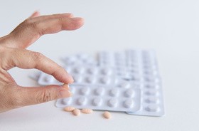 Ręka pacjenta trzyma pół tabletki statyn i biały blister na białym tle, lek do leczenia hiperlipidemii lub obniżenia poziomu cholesterolu we krwi