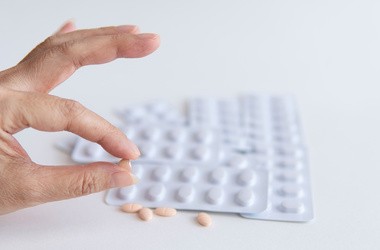 Ręka pacjenta trzyma pół tabletki statyn i biały blister na białym tle, lek do leczenia hiperlipidemii lub obniżenia poziomu cholesterolu we krwi