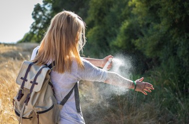 Kobieta podczas wycieczki spryskuje swoją skórę repelentem na komary