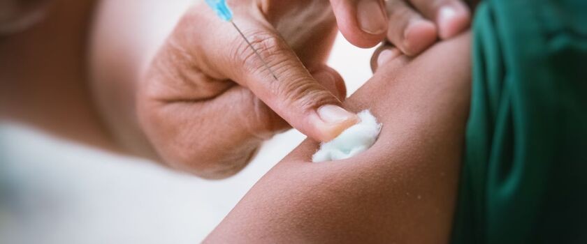Podanie szczepionki na krztusiec. Ręka medyka dociskająca wacik na ramieniu zaszczepionego pacjenta. szczepienie krztusiec
