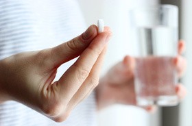 Kobieta trzyma w dłoni tabletkę z apsiryną a w drugiej szklankę wody