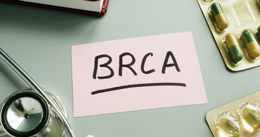 Napis BRCA na kawałku papieru, który leży na stole obok stetoskopu i tabletek