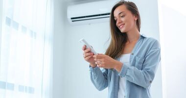 Kobieta ustawiająca klimatyzację. Czym grozi nieczyszczona klimatyzacja?