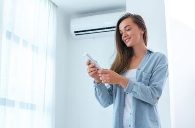 Kobieta ustawiająca klimatyzację. Czym grozi nieczyszczona klimatyzacja?