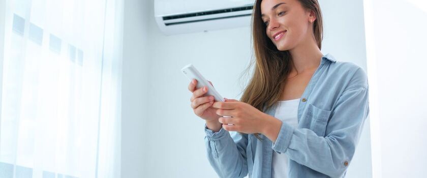 Kobieta ustawiająca klimatyzację. Czym grozi nieczyszczona klimatyzacja?