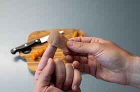 Dłonie opatrujące ranę od noża. Skaleczenie, drobne urazy skóry, siniaki, jak opatrzyć skaleczenie.