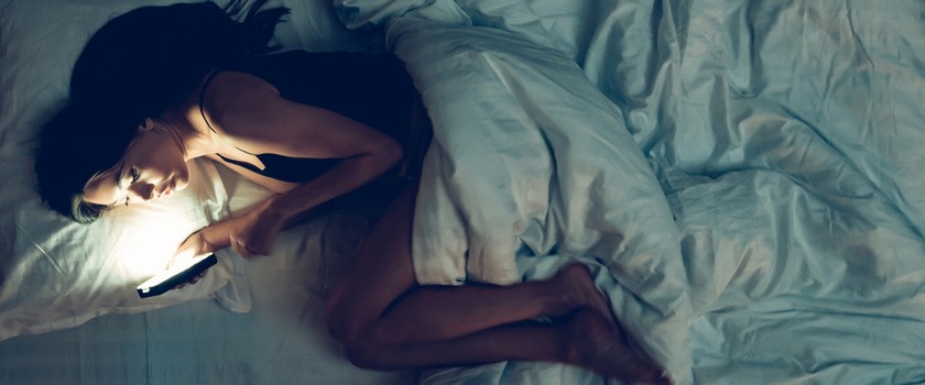 Kobieta leży w łóżku i korzysta ze smartfona
