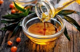 Olej z rokitnika lejący się z butli do miski, owoce rokitnika.