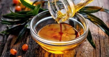 Olej z rokitnika lejący się z butli do miski, owoce rokitnika.