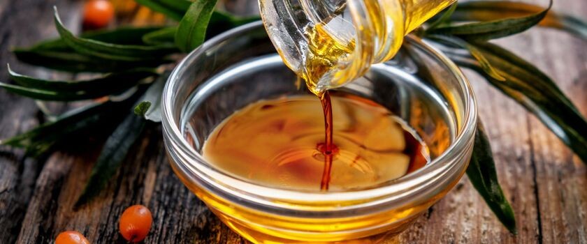 Olej z rokitnika lejący się z butli do miski, owoce rokitnika.