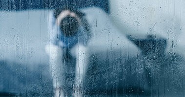 Osoba w depresji za szybą w deszczowy dzień