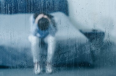 Osoba w depresji za szybą w deszczowy dzień