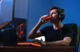 Młody męzczyzna pije napój energetyczny przed komputerem