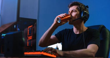Młody męzczyzna pije napój energetyczny przed komputerem